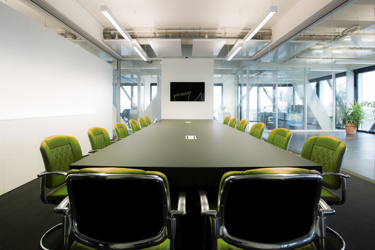 heller Konferenzraum mit grünen Stühlen und großem Tisch mit eingebauter Technik
