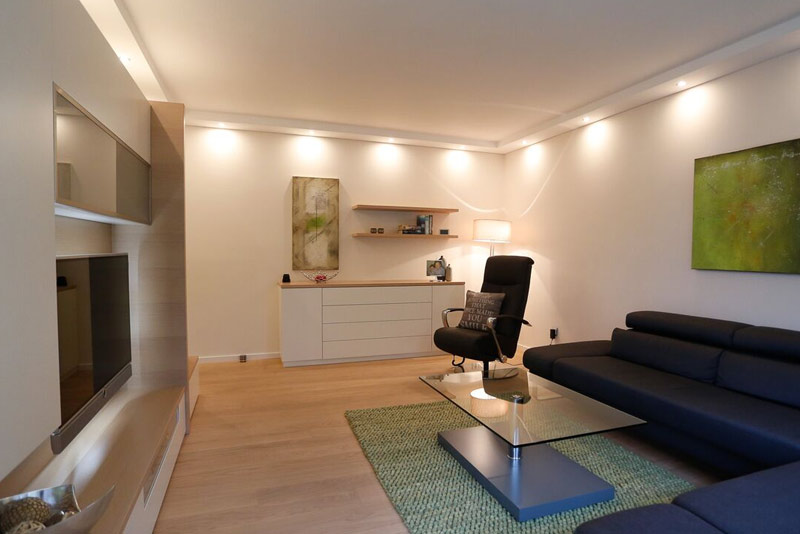 gemütliches Wohnzimmer mit Ecksofa, indirekter Beleuchtung und schreinergefertigten Möbel